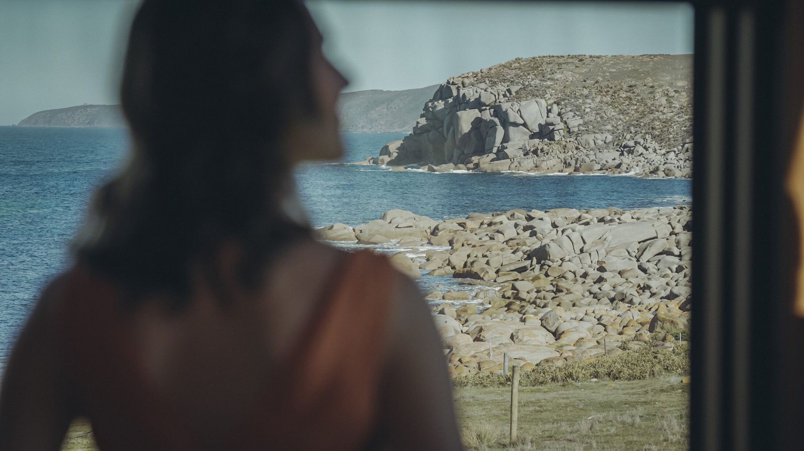 A guest looking out at the boulder-strewn Kangaroo Island shoreline from inside a retreat