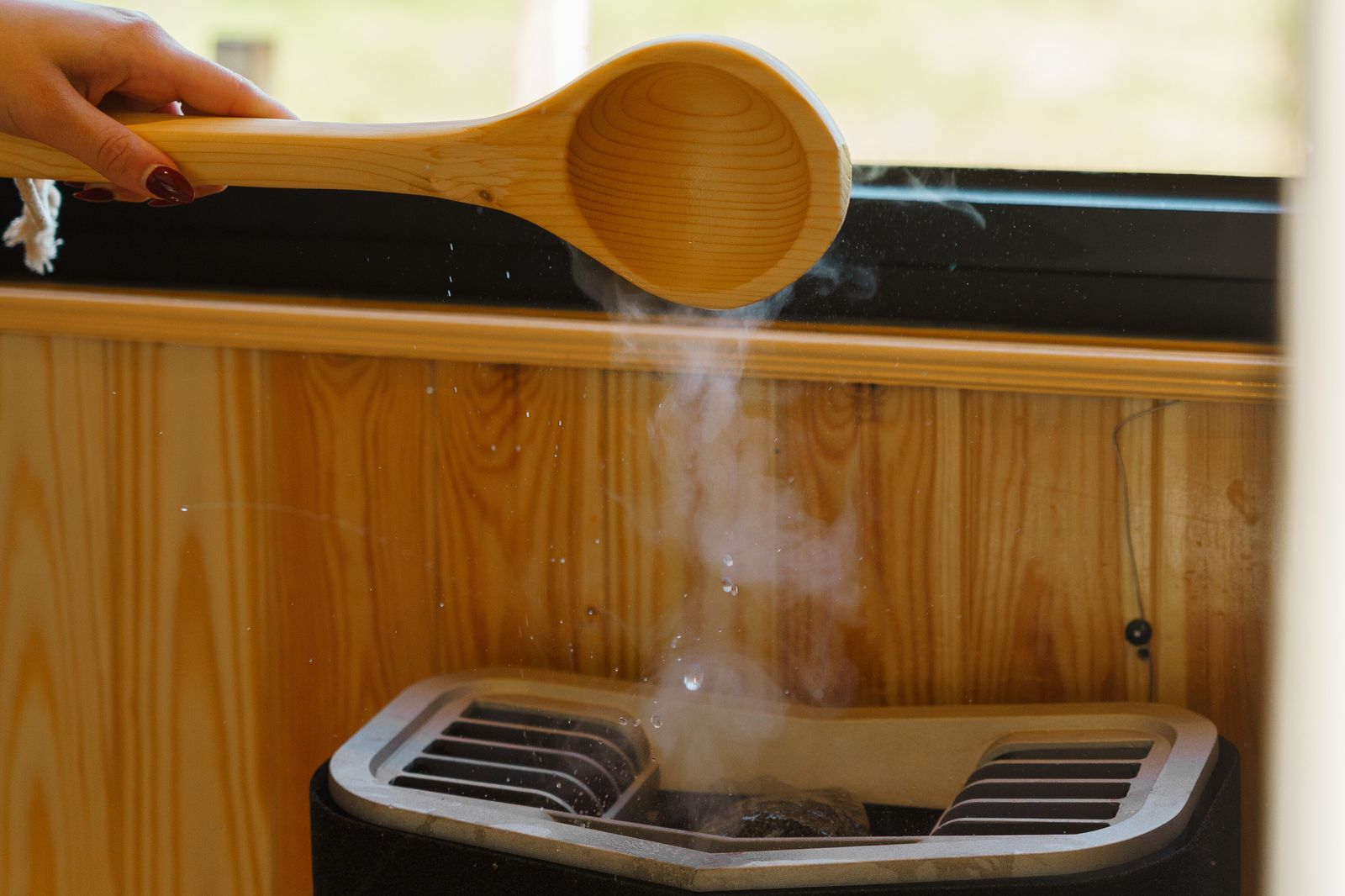A wooden ladle pouring water over the hot stones of a retreat sauna, steam rising