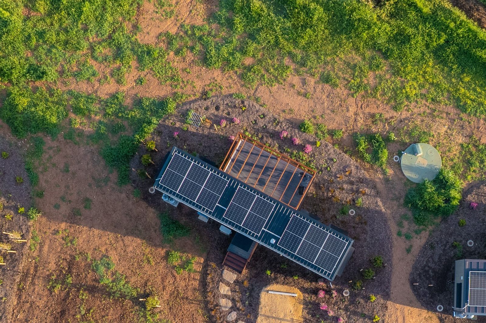 Overhead view of a completed AUTRA module installed on its site, solar roof and timber pergola frame above freshly planted ground